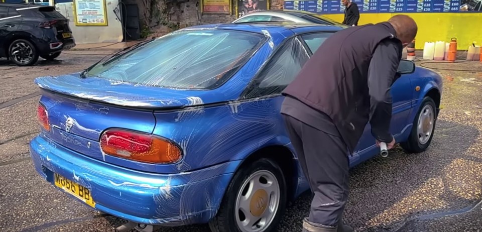 a man is washing a blue car with a license plate that says ln88 bb