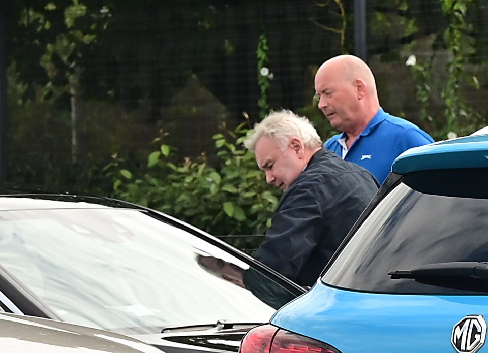 two men are standing next to a blue mg car