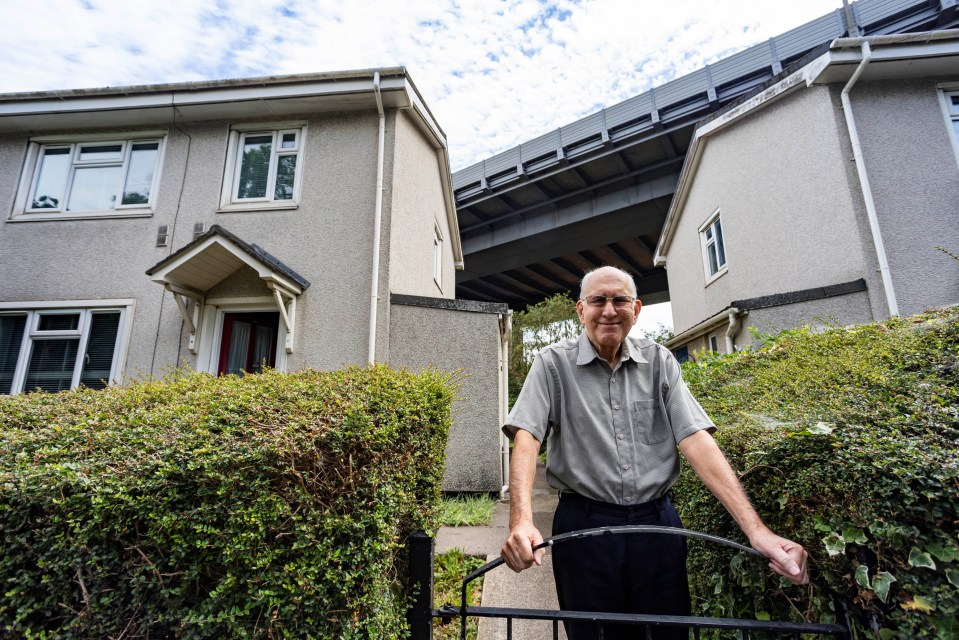 a man stands in front of a house with a bridge in the background