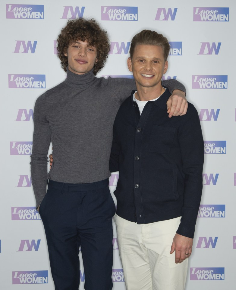 two men pose in front of a wall that says loose women