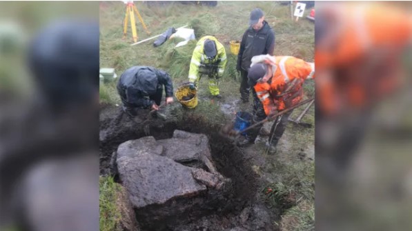 a group of people are digging in the dirt near a large rock .