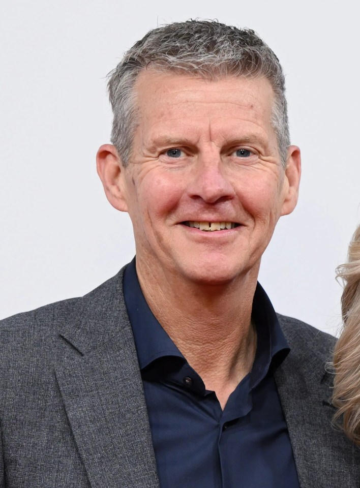 a man in a suit and a woman in a black dress pose on a red carpet