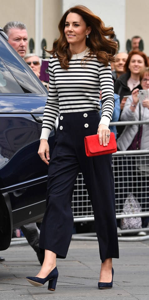 a woman wearing a striped top and black pants holds a red clutch