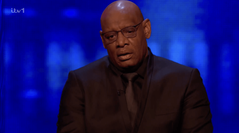 a man in a suit and tie is sitting in front of a blue screen that says itv1