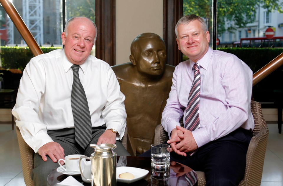 two men sit at a table with a statue in the background