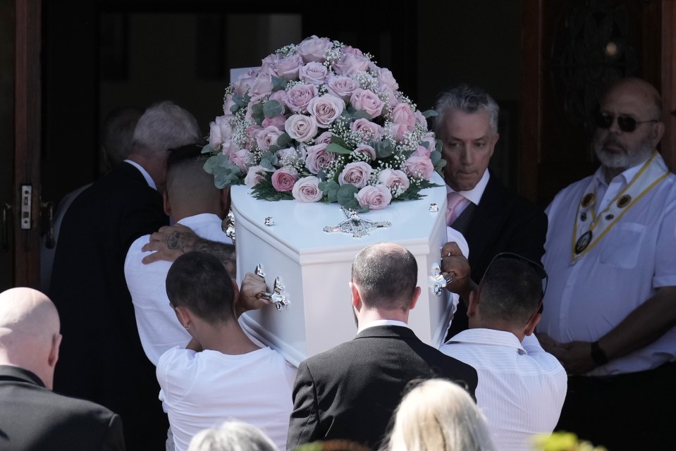 men carry a white coffin with pink roses on it