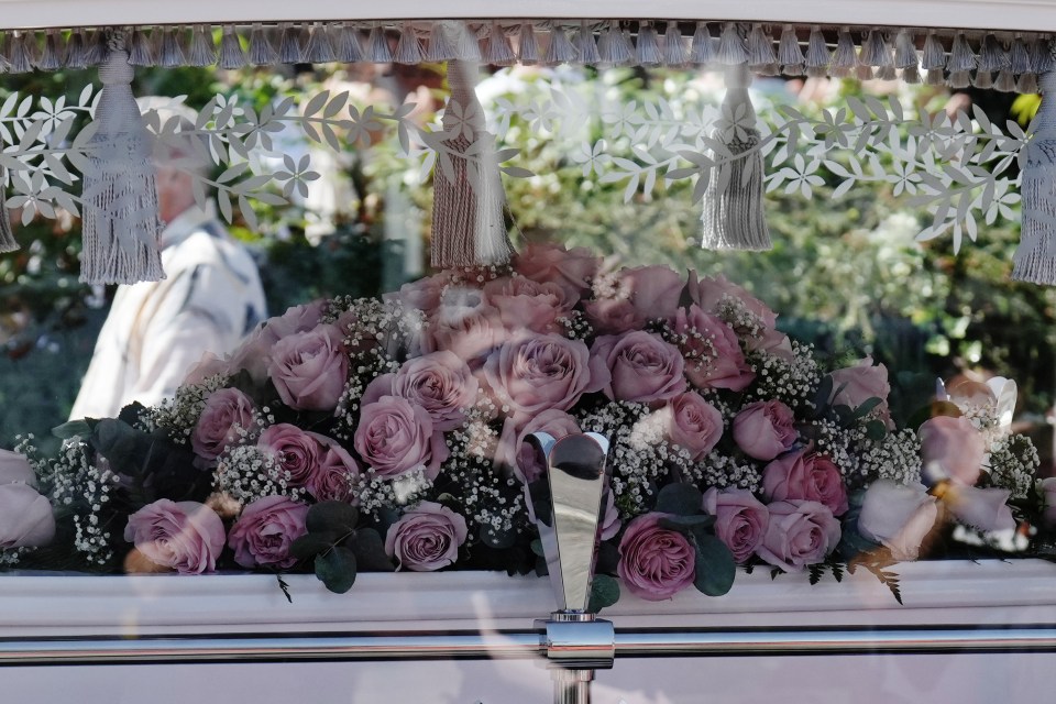 a white coffin with pink roses and baby 's breath