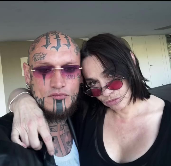 a woman wearing red sunglasses stands next to a man with a tattoo on his head that says xii