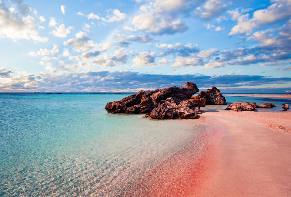 a beach with pink sand and rocks in the water