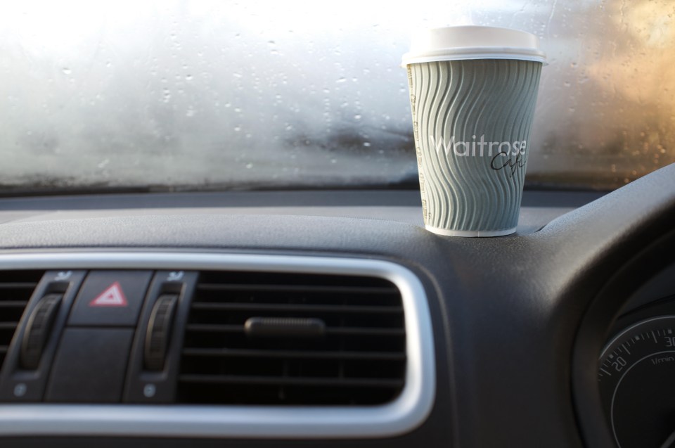 a cup of waitrose coffee sits on the dashboard of a car