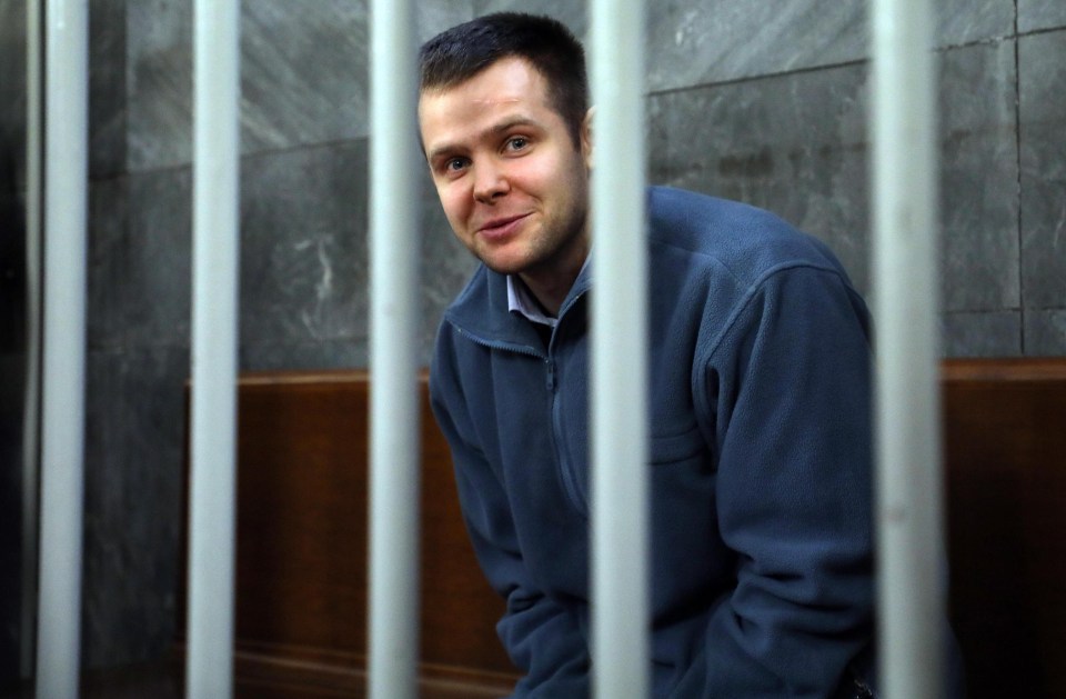 a man in a blue sweater is smiling behind bars