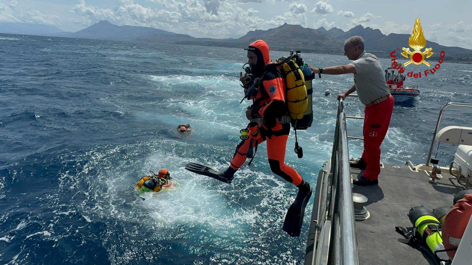 Divers plunge into the waters near the site of the wreck on Tuesday