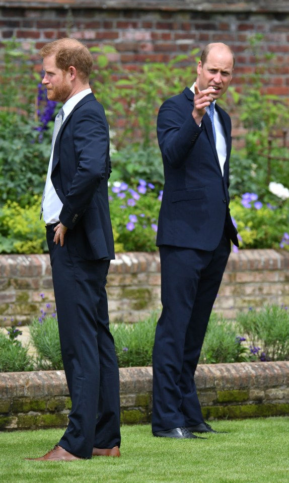 two men in suits standing next to each other in a garden