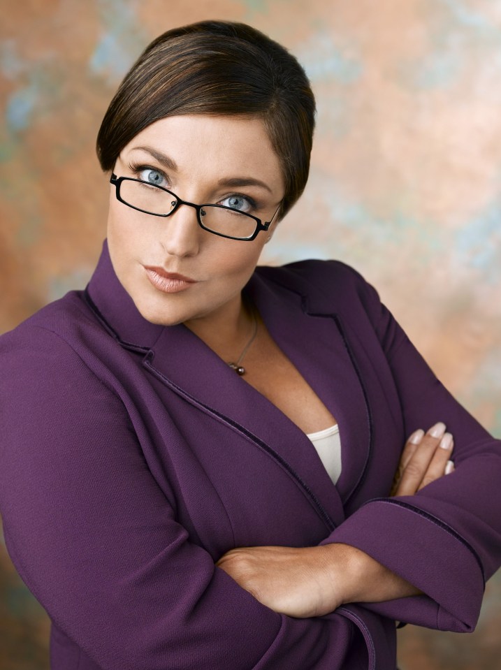 a woman wearing glasses and a purple suit has her arms crossed