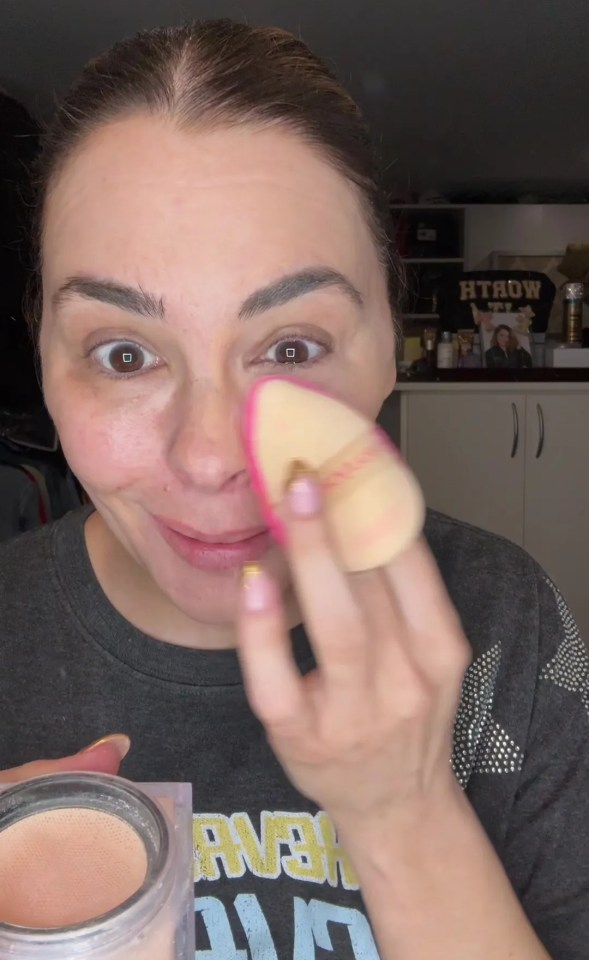 a woman wearing a htrow shirt is applying makeup