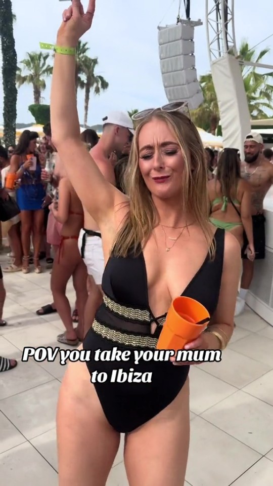 a woman in a black swimsuit is holding an orange cup with the caption pov you take your mum to ibiza