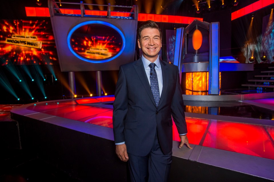 a man in a suit and tie stands in front of a stage with a sign that says ' who wants to win '