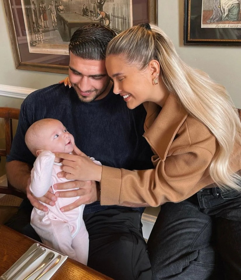 a man and woman holding a baby in front of a framed picture of a pool table