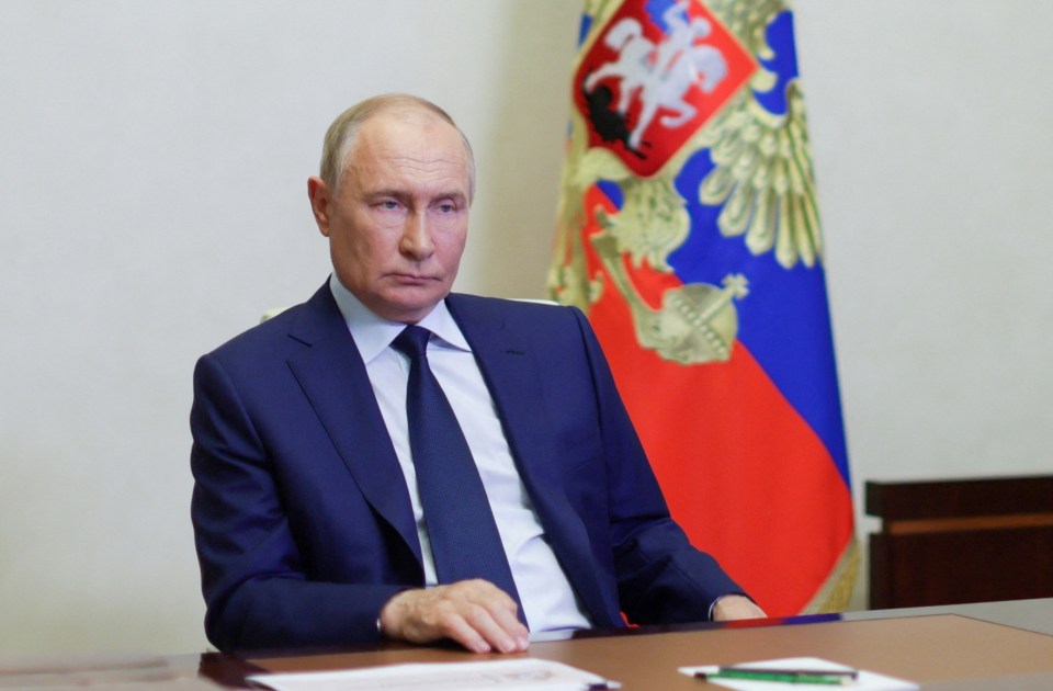 a man in a suit and tie sits at a desk in front of a russian flag