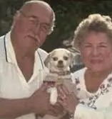 an elderly couple is holding a small dog in their arms .