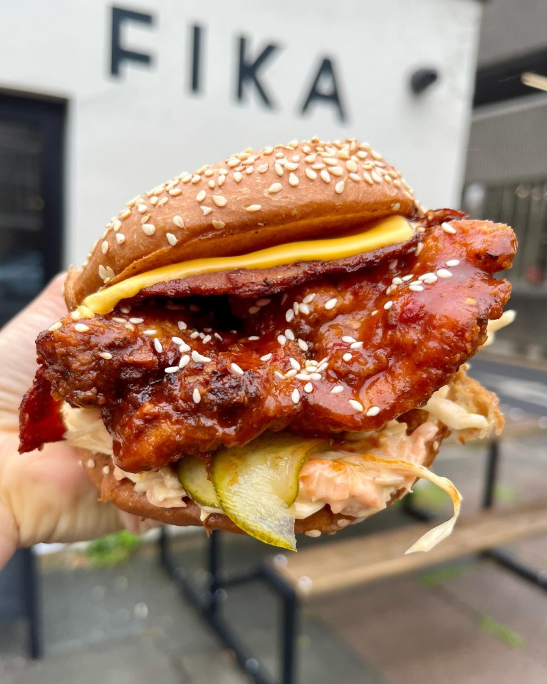 a person is holding a chicken sandwich in front of a sign that says fika