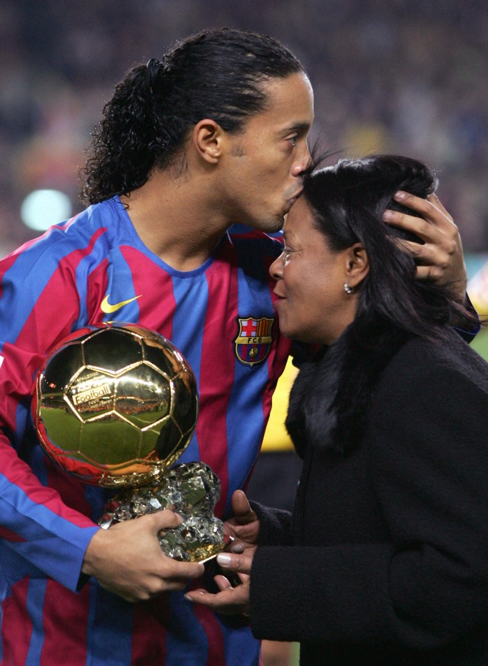 a soccer player kisses his mother while holding a trophy