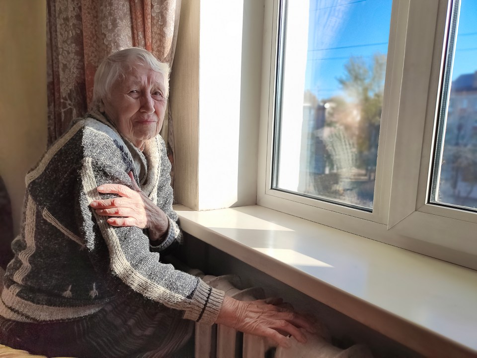 an elderly woman sitting on a window sill looking out