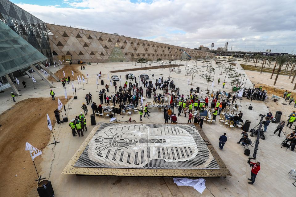 People gather around a depiction of the ancient Egyptian Pharaoh Tutankhamun’s death mask made of 7260 cups of coffee, in front of the newly-built Grand Egyptian Museum