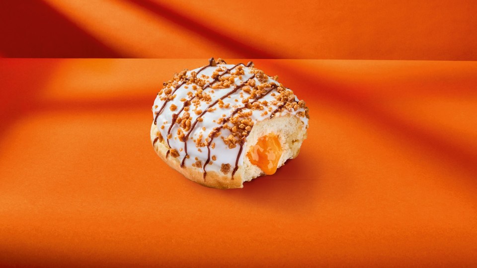 a donut with a bite taken out of it sits on an orange surface