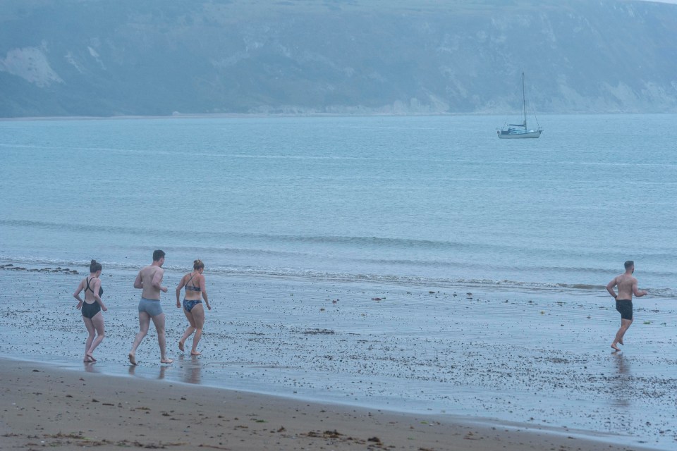 a group of people running on a beach with a sailboat in the background