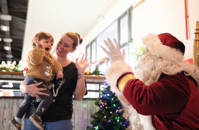 a woman holds a child while talking to santa claus