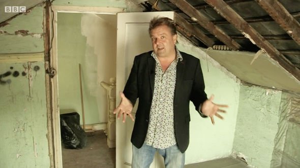 a man in a suit is standing in an attic with his arms outstretched .