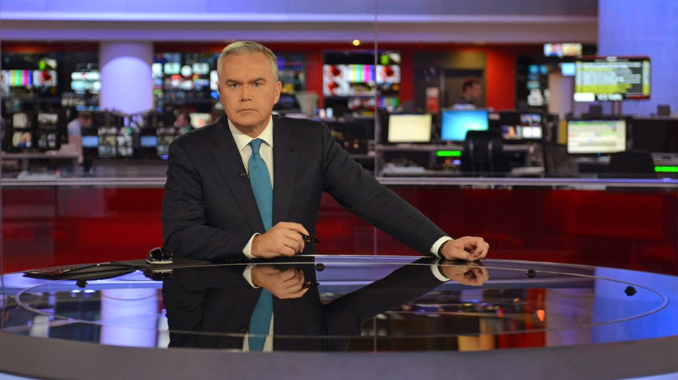 a man in a suit and tie stands at a news desk