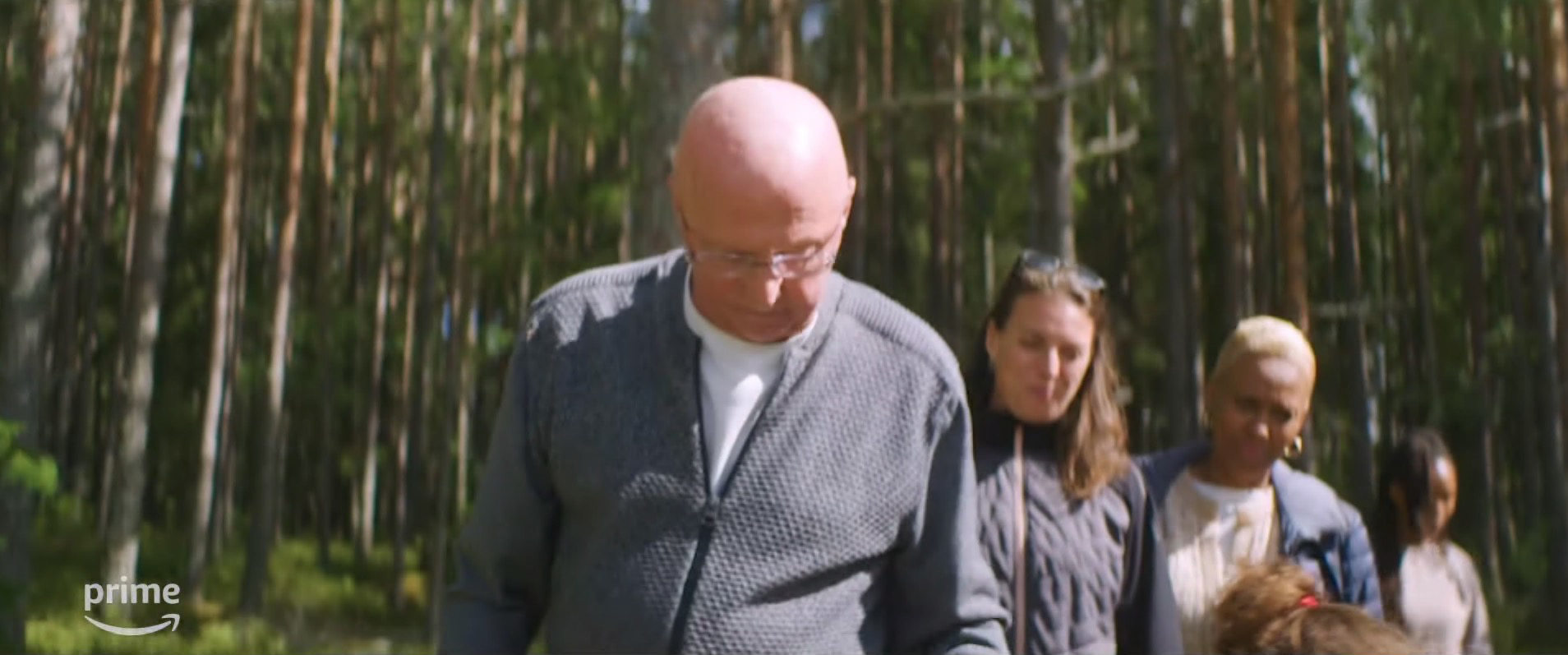 a group of people walking through a forest with a prime logo in the corner