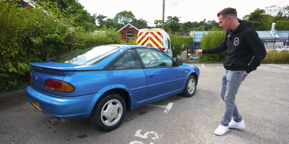 a man is standing next to a blue car that has a license plate that says jcw