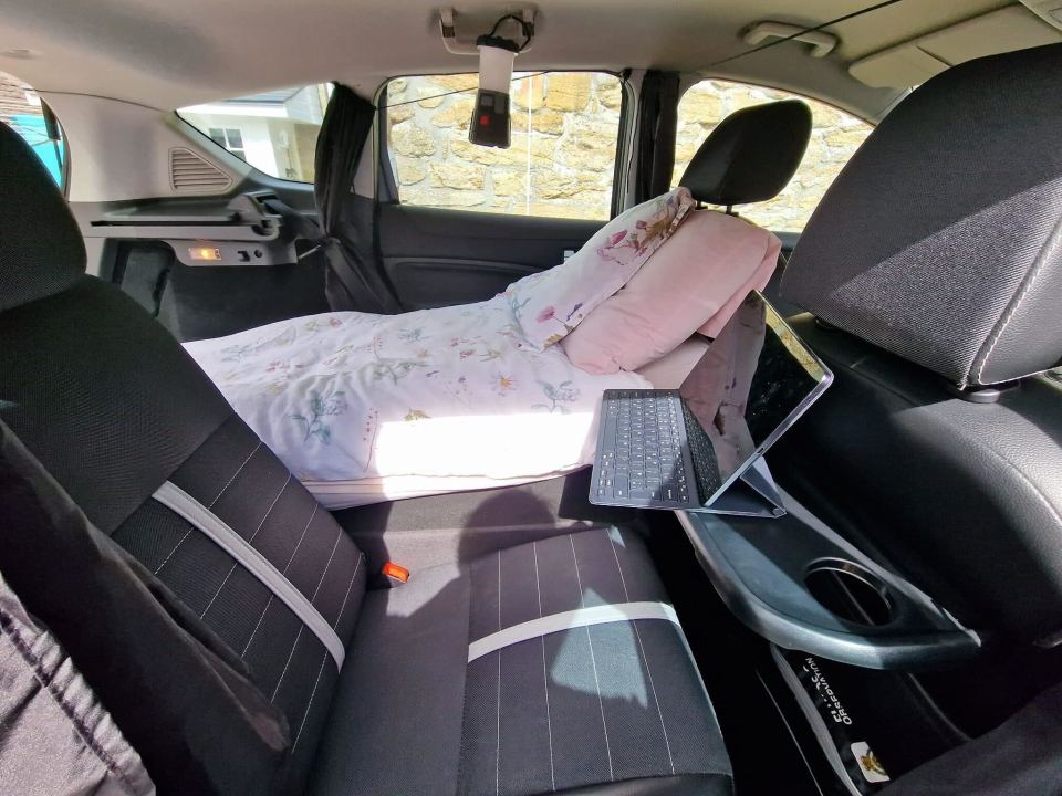 a car with a bed and a laptop on the back seat