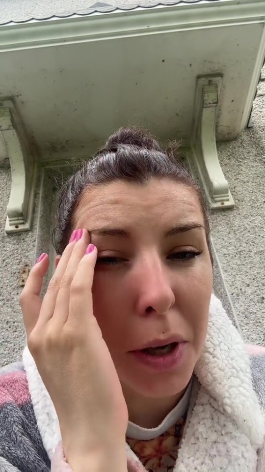 a woman with pink nails wipes her eye with her hand