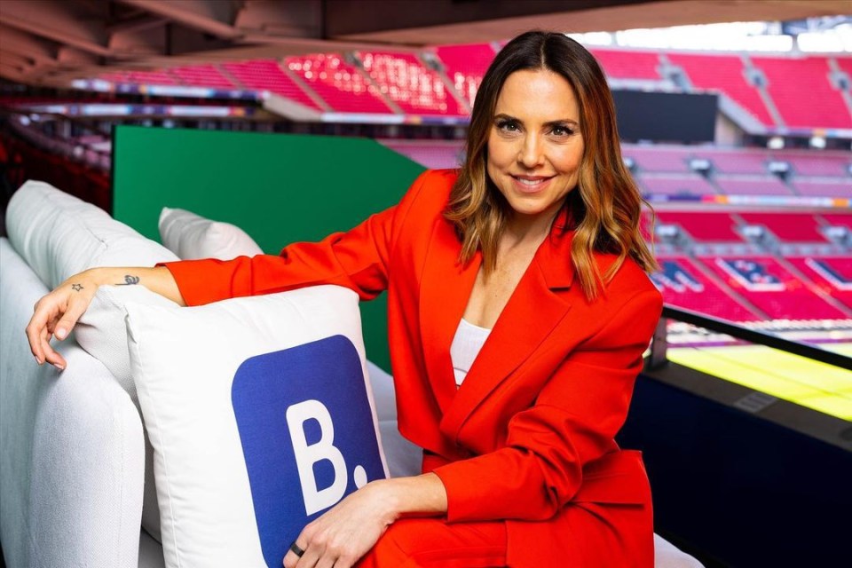 a woman in a red suit sits on a couch with a blue pillow with the letter b on it