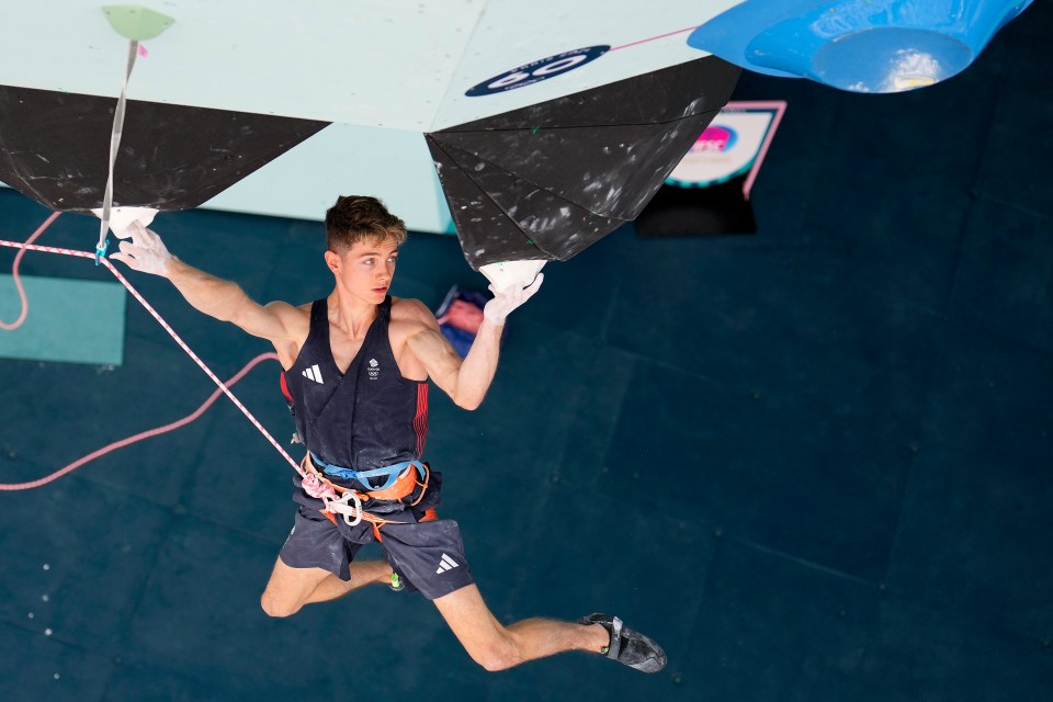 a man in an adidas tank top is climbing a wall