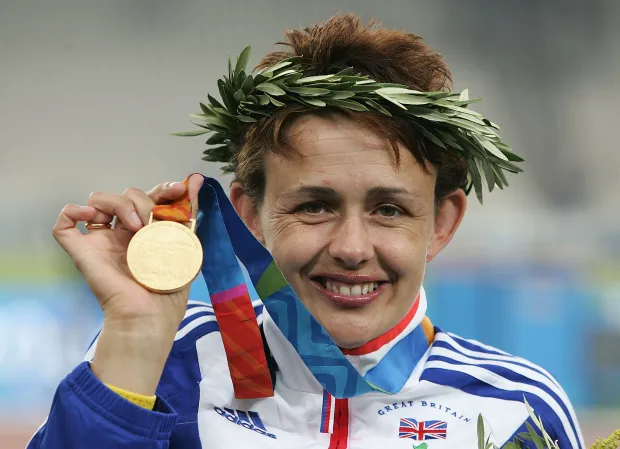 a woman in a great britain jacket holds up her gold medal