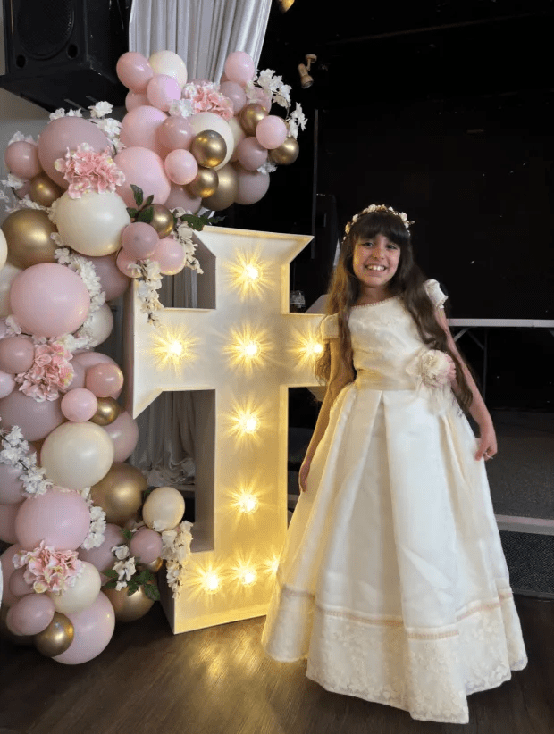 a little girl in a white dress stands in front of a large letter f