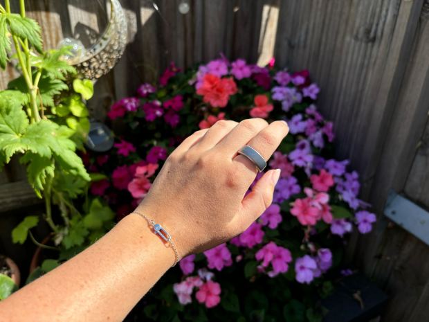 a woman wearing a ring and a bracelet stands in front of flowers