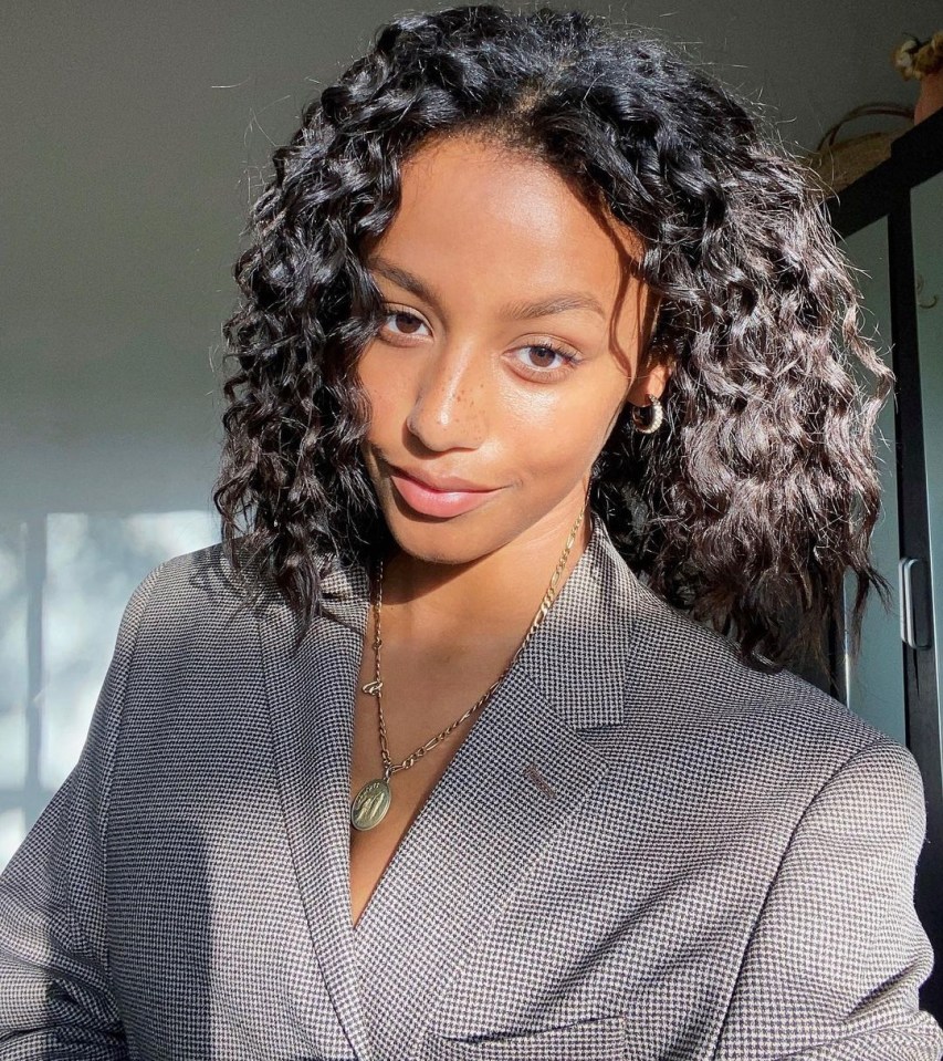 a woman with curly hair is wearing a jacket and necklace