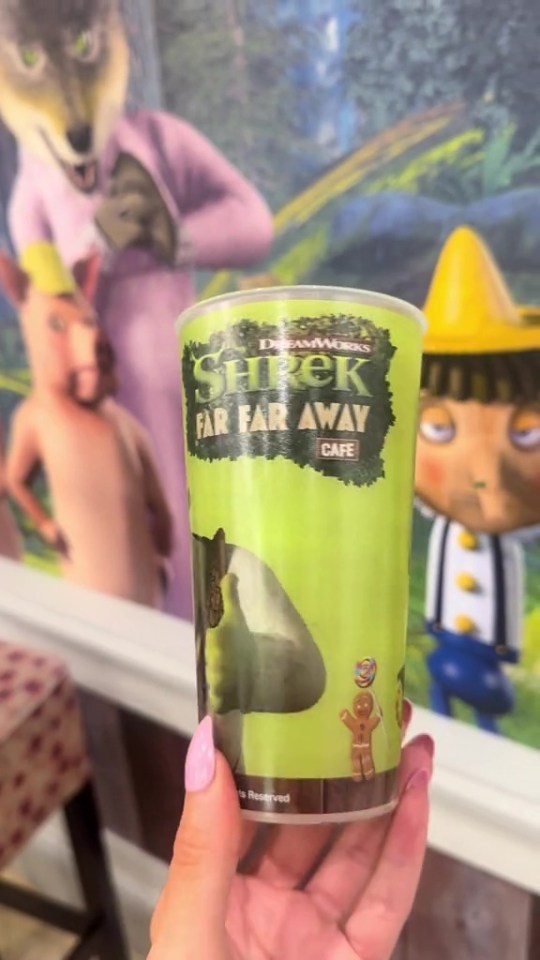 a person holding a cup that says shrek far far away cafe