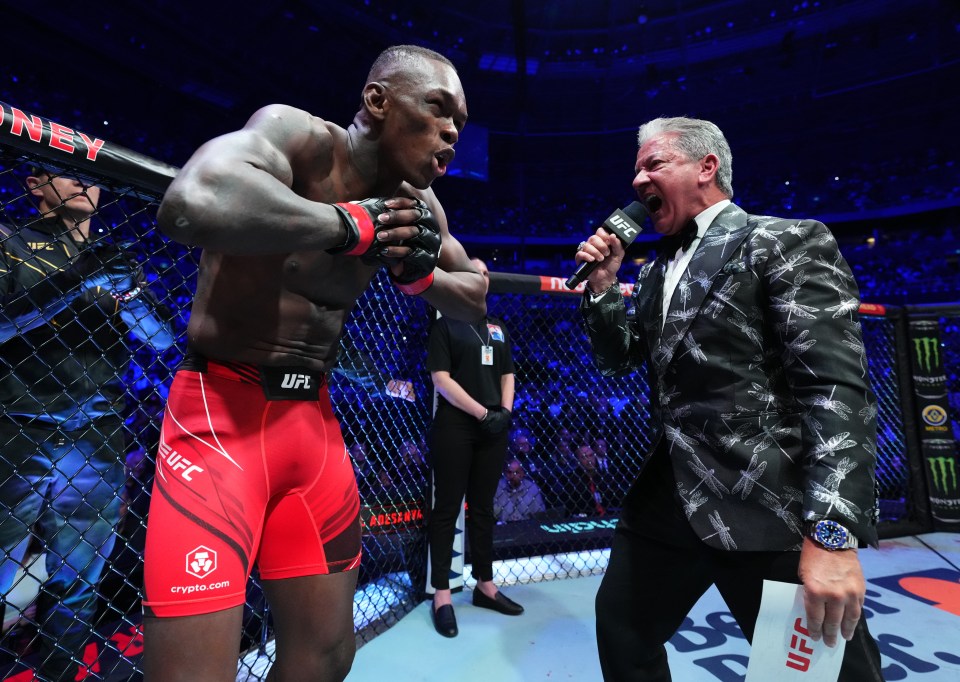 a man in a suit is talking into a microphone while a man in a ufc uniform stands behind him