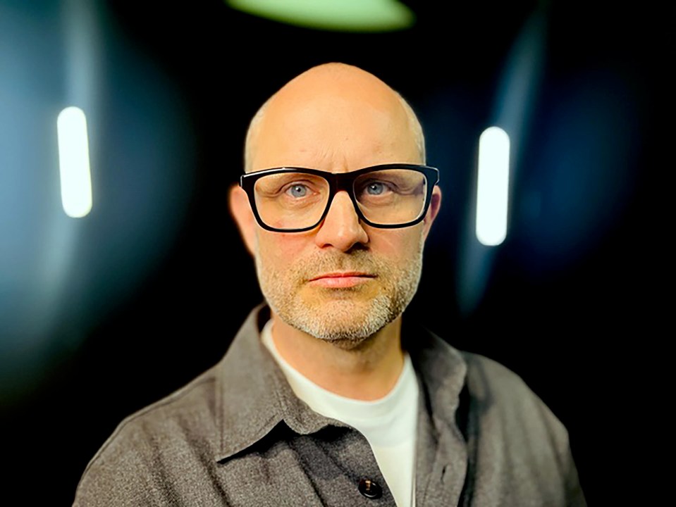 a bald man with glasses and a beard looks at the camera