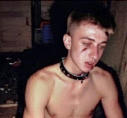 a shirtless young man with a choker around his neck is sitting in a dark room .