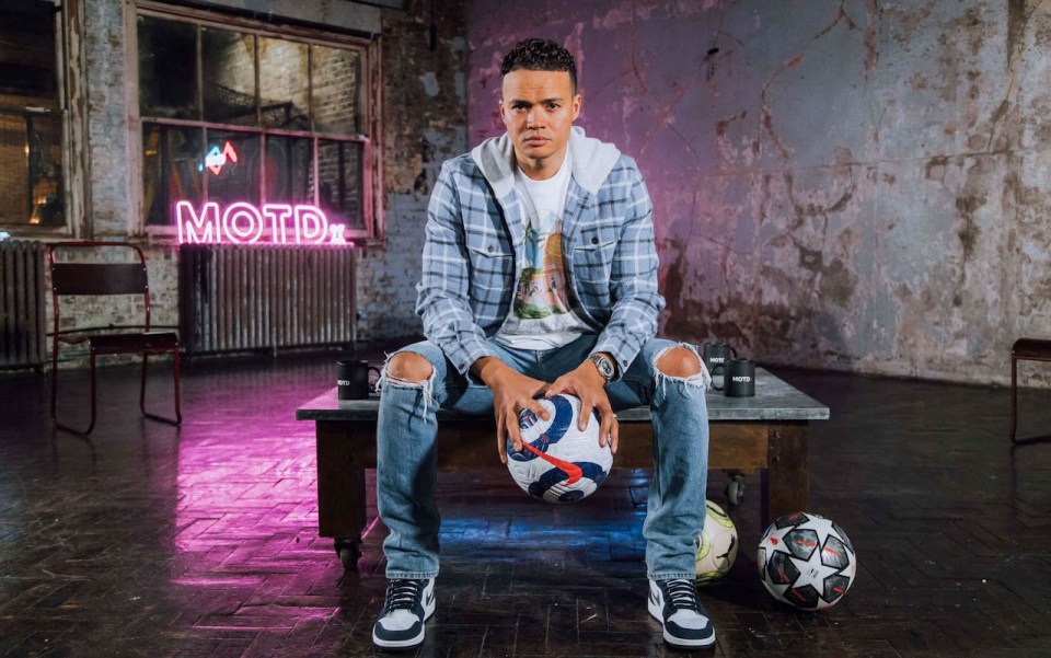 a man sits on a table with a soccer ball in front of a neon sign that says motd