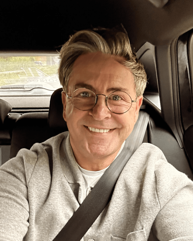 a man wearing glasses and a seat belt smiles for the camera