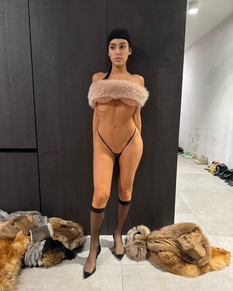 a woman in a fur crop top stands next to a pile of fur coats